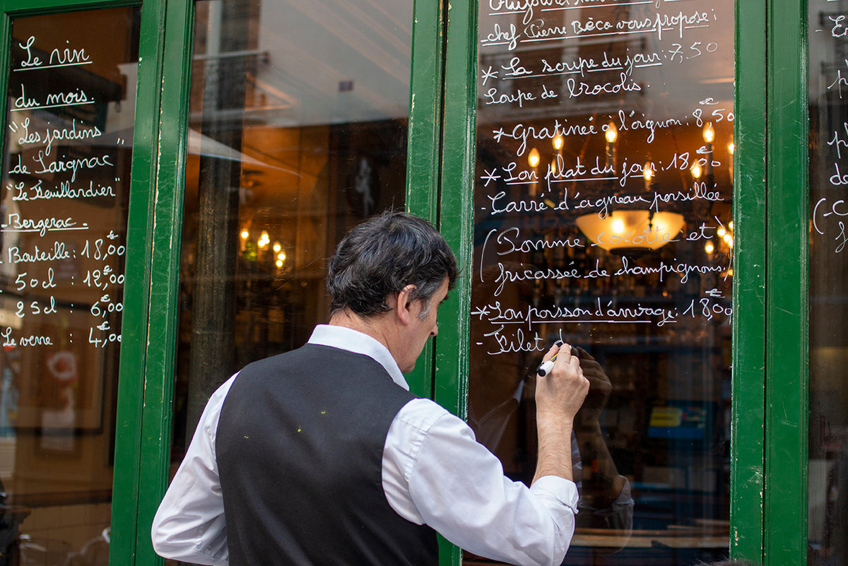 Classic French Bistro and Waiter Writing Daily Menu on Chalkboard